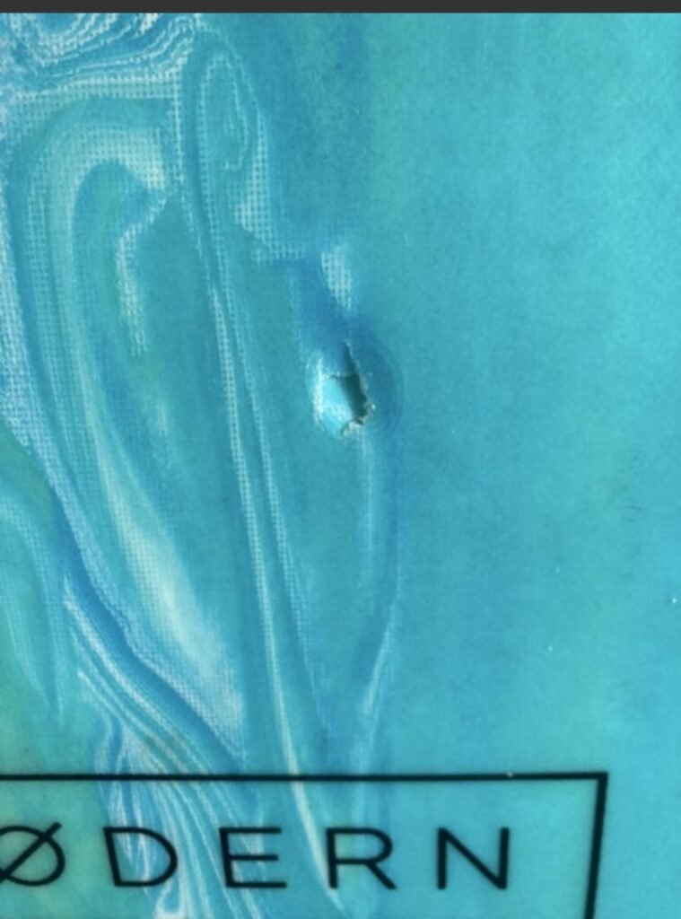 Gros plan sur un trou percé dans la fibre de verre d'une planche bleue, fond de mousse visible