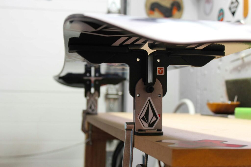 Nez d'un snowboard maintenu dans un étau d'atelier, gros plan sur la fixation de bord
