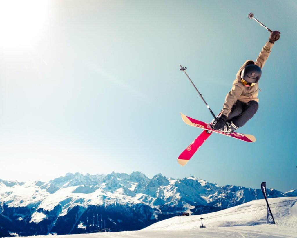 Skieur freestyle en plein saut, skis croisés, dans les Alpes sous un ciel dégagé