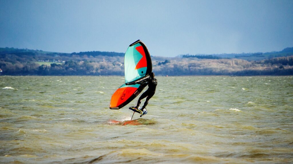 Wingfoiler en plein vol au-dessus de l'eau sur un hydrofoil, voile bicolore gonflée